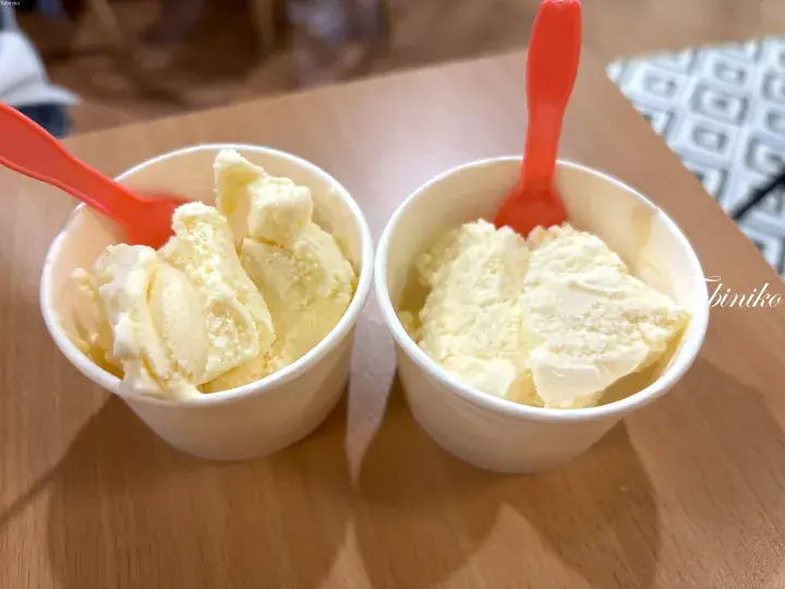Two white cups of creamy yellow ice cream with red spoons on a wooden table.