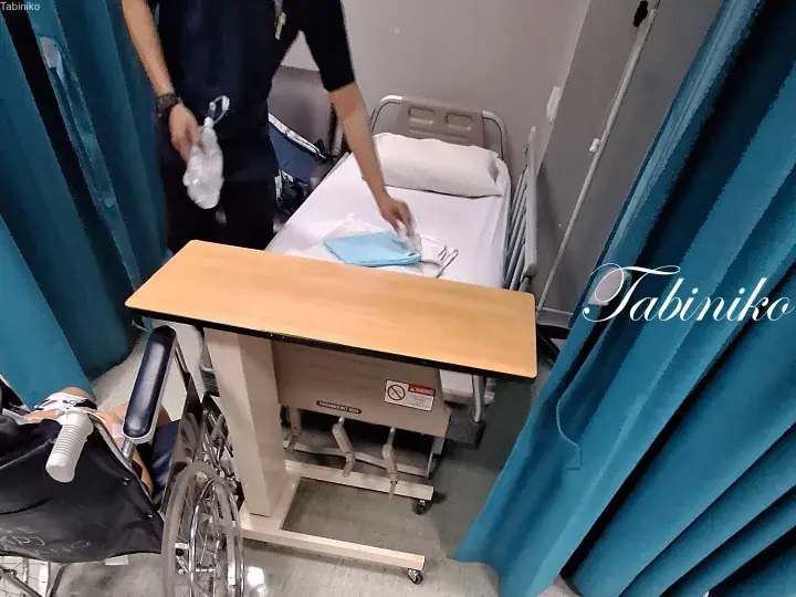 Hospital staff preparing a bed with linens in a private room with blue curtains and a wheelchair nearby.