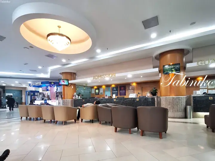 Spacious hospital admission lobby with beige armchairs, a ZUS Coffee kiosk, and a reception counter.