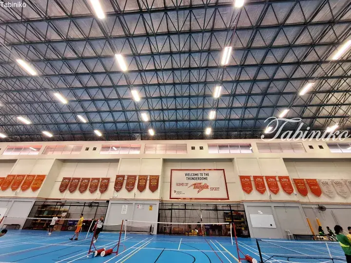 Indoor sports hall at Taylor’s International School featuring blue badminton courts and championship banners.
