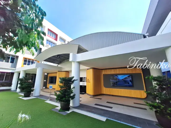 Modern building entrance with curved white canopy, wooden feature wall, and landscaped green lawn.