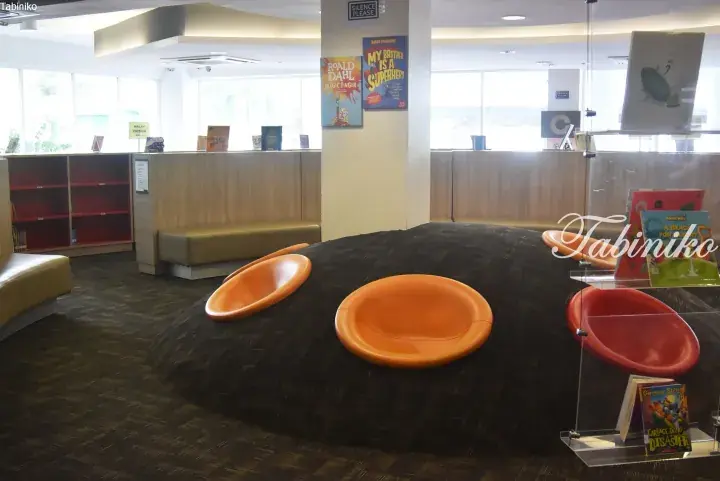 Children’s reading area with orange pod seats on a dark carpeted mound in a modern library.
