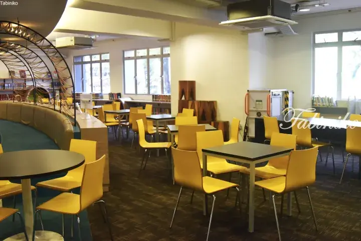 Modern library interior with yellow chairs, round tables, and a curved seating area under a decorative arch.