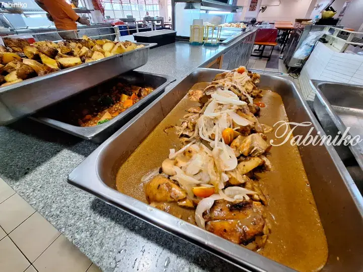 Buffet trays of roasted potatoes, vegetable stew, and chicken in brown sauce with onions at a Malaysian restaurant.
