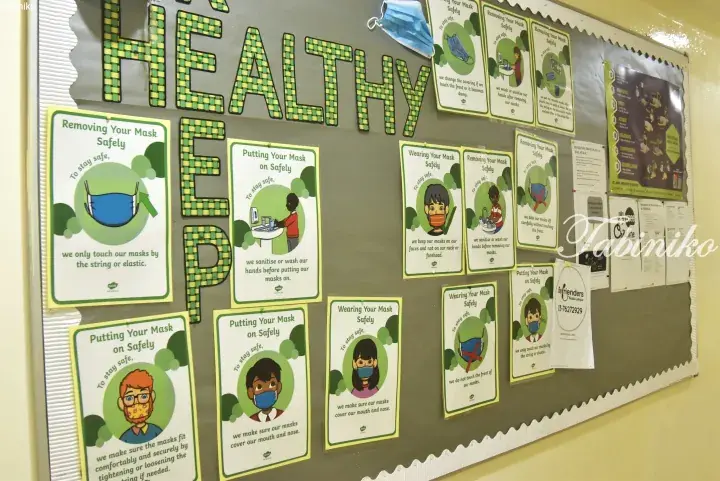 Bulletin board displaying health posters about safe mask wearing and removal procedures in a Malaysian facility.