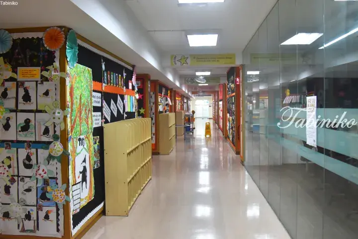 Bright school hallway with student artwork on display boards and wooden shelves along the corridor.