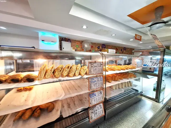Display case filled with various pastries like chocolate rolls and chicken curry puffs at a Malaysian bakery.