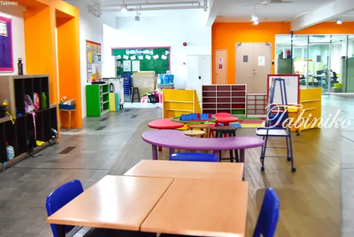 Colorful classroom with orange walls, child-sized tables, chairs, and storage shelves in a modern learning space.