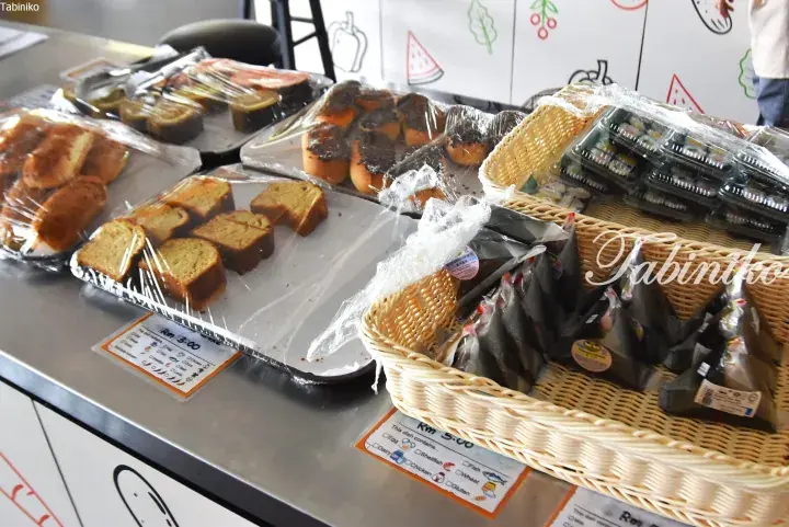 Assorted packaged cakes and onigiri displayed on a stainless steel counter at a Malaysian food stall.