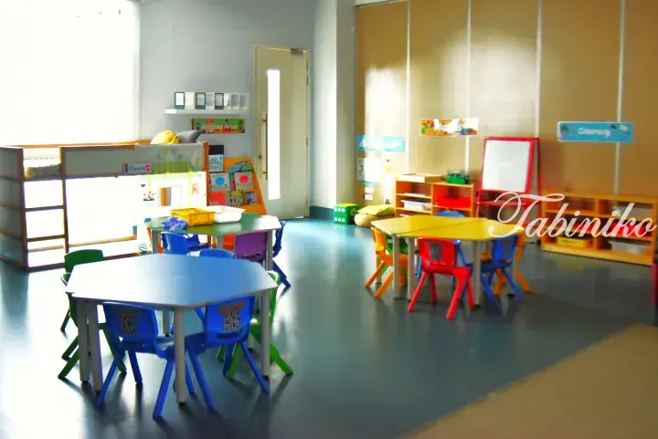 Colorful children’s play area with small tables, chairs, and reading corner in a bright room.