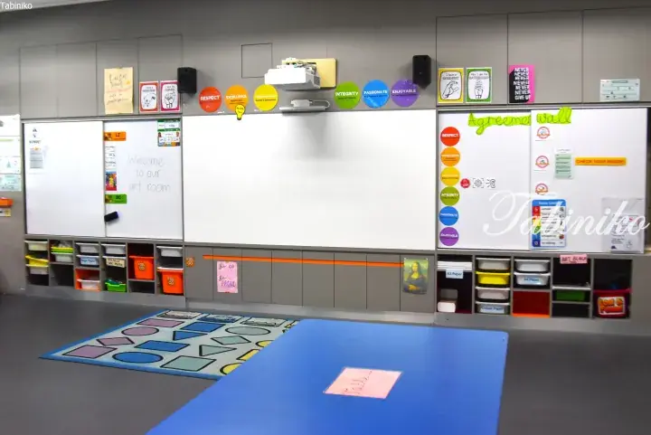 Modern classroom with whiteboards, colorful educational posters, and organized storage bins along the wall.