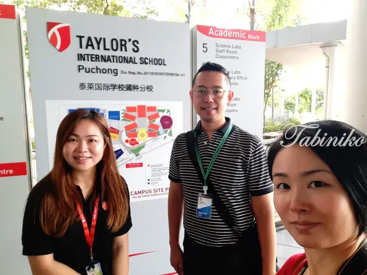 Three people standing in front of a sign for Taylor’s International School Puchong campus.