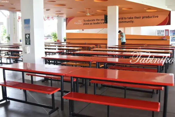 Empty school cafeteria with red tables and benches, orange walls, and a mission statement banner.