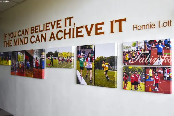 Motivational quote “If you can believe it, the mind can achieve it” by Ronnie Lott displayed above student sports photos in a school hallway.