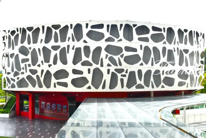 Modern building with a perforated white facade and red base, featuring a glass canopy entrance.
