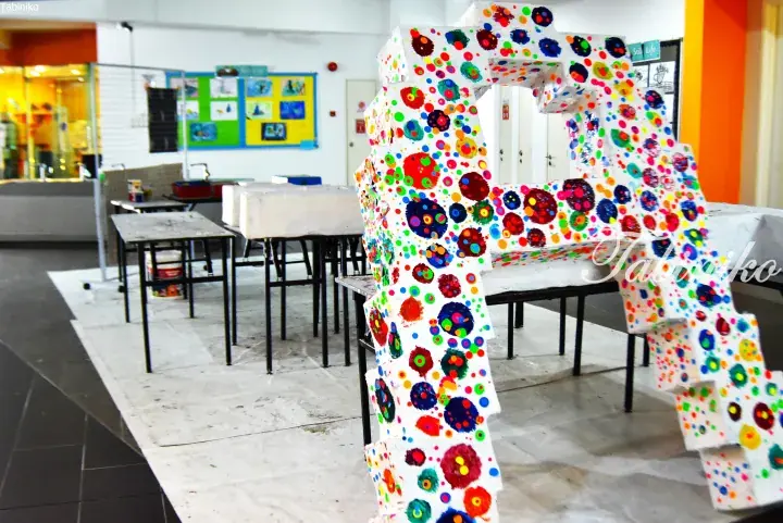 Colorful polka dot art installation in a bright classroom with tables and student artwork on walls.