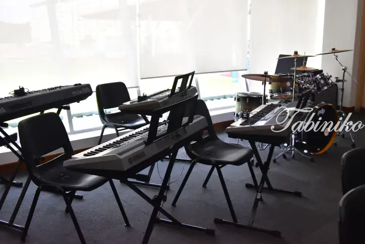 Music studio with Yamaha keyboards and a drum set near large windows.