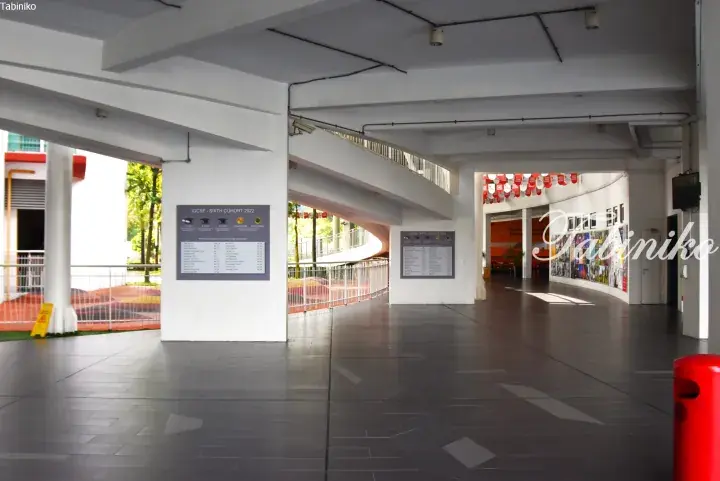 Modern school corridor with white pillars, notice boards, and a spiral staircase.