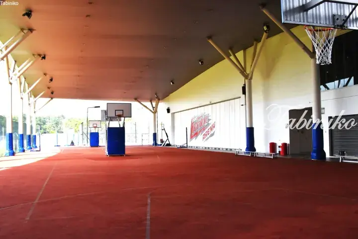 Empty red basketball court at Taylor’s Lightning Arena with blue pillars and hoops under a covered roof.