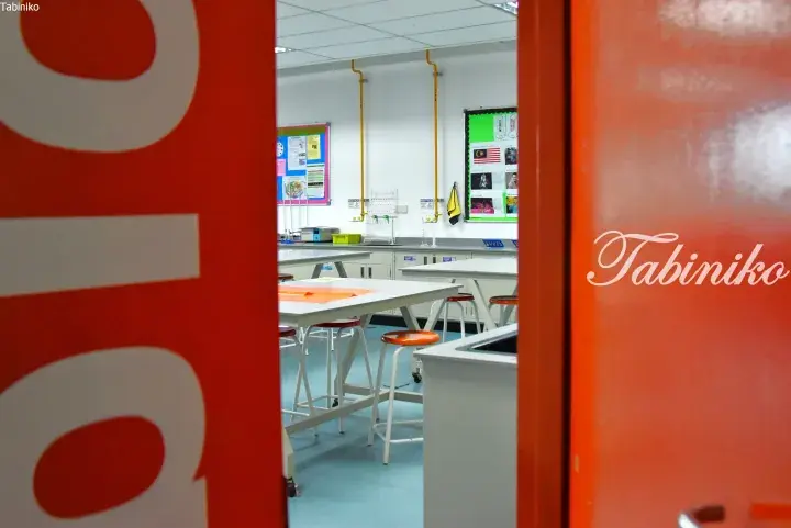 View into a modern science classroom with white tables, orange stools, and a Malaysian flag on the bulletin board.
