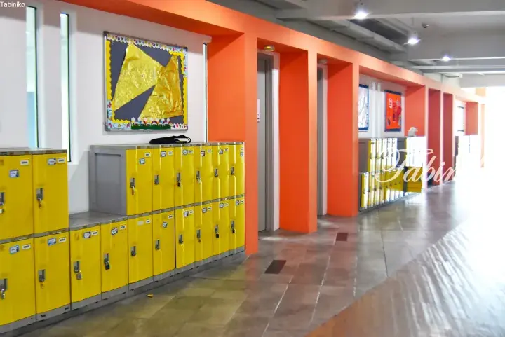 Bright yellow lockers line a hallway with orange pillars and a bulletin board in a modern building.