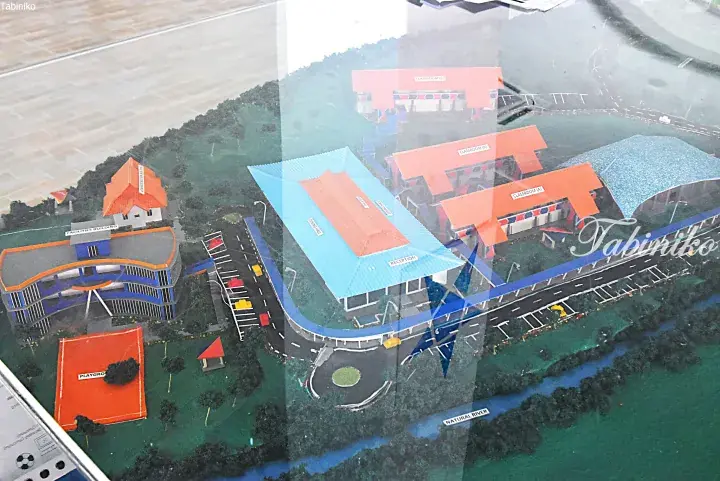 Architectural model of a modern school complex featuring classrooms, a dining hall, and a playground near a river.