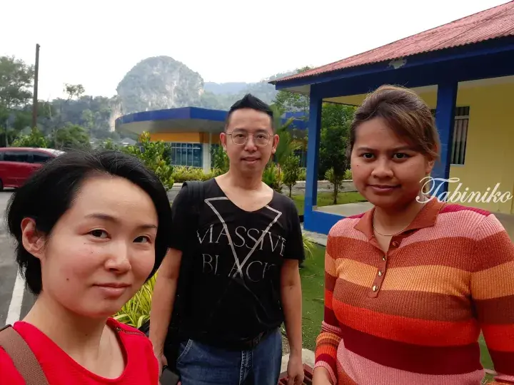 Three travelers pose for a selfie with a limestone hill and colorful building in the background.