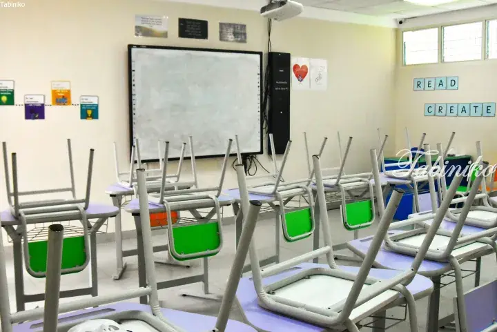 Empty classroom with chairs stacked on desks, whiteboard, and READ CREATE wall signs.