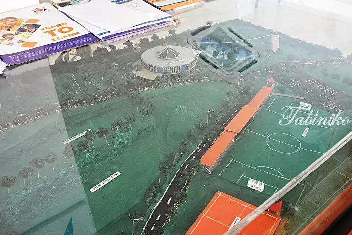 Architectural model of a school campus featuring a circular building, soccer fields, and a brochure titled ‘Yearn to Learn’.