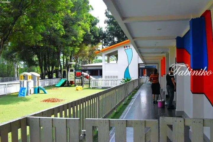 Colorful playground with slides and climbing structures on green turf next to a building corridor with red and blue wall art.