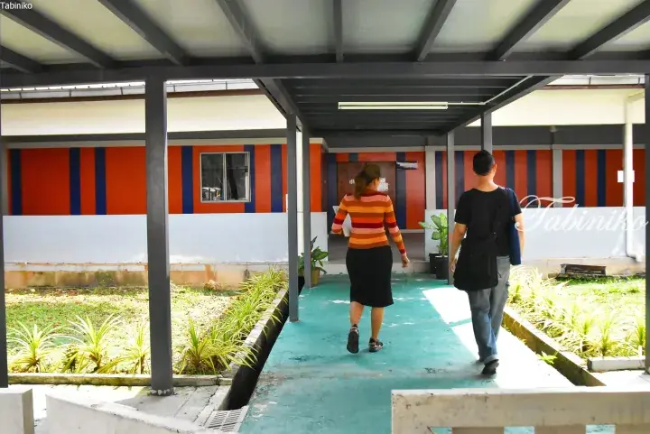 A couple walks along a teal pathway under a covered walkway at a property with orange and blue striped walls.