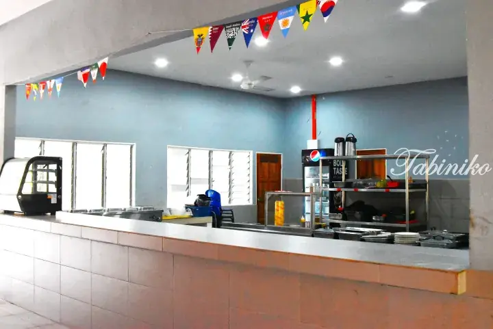 Empty cafeteria counter with food warmers and international flags hanging from the ceiling.