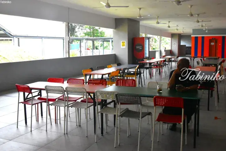 Colorful chairs and tables in a bright open-air dining area with ceiling fans and a view of greenery outside.