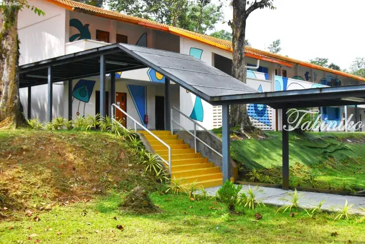 White resort building with yellow stairs and blue abstract murals on a grassy hillside in Malaysia.