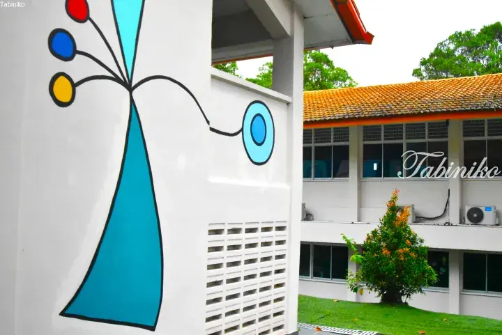 Colorful abstract mural on a white wall outside a building with a tiled roof in Malaysia.