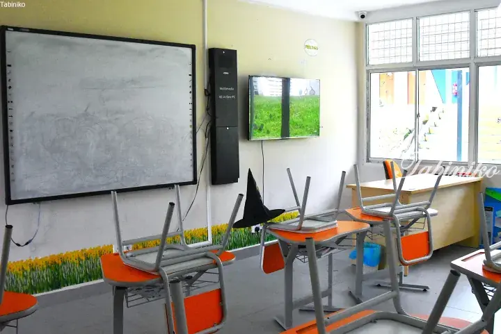 Classroom with orange chairs stacked on desks, a smartboard, and a TV screen showing a grassy field.