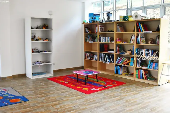 Bright children’s reading corner with colorful rugs, low table, and bookshelves filled with educational books.
