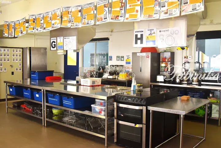 Modern commercial kitchen with stainless steel counters, ovens, and labeled cooking stations.