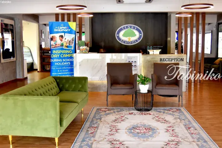 Modern reception area of Tenby Schools with green sofa, brown armchairs, and a Camp Beaumont banner.