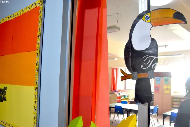 Colorful toucan cutout decoration on a classroom window with orange and yellow wall displays.