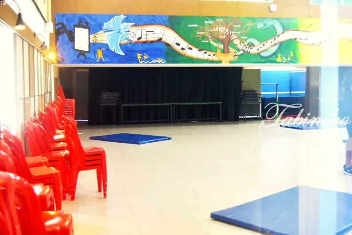 Red chairs in a hall with a stage and a colorful mural featuring a dragon and tree.