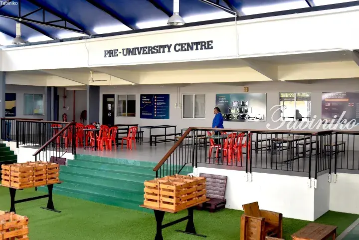 Pre-University Centre exterior with green steps, red chairs, and wooden tables in a covered walkway.