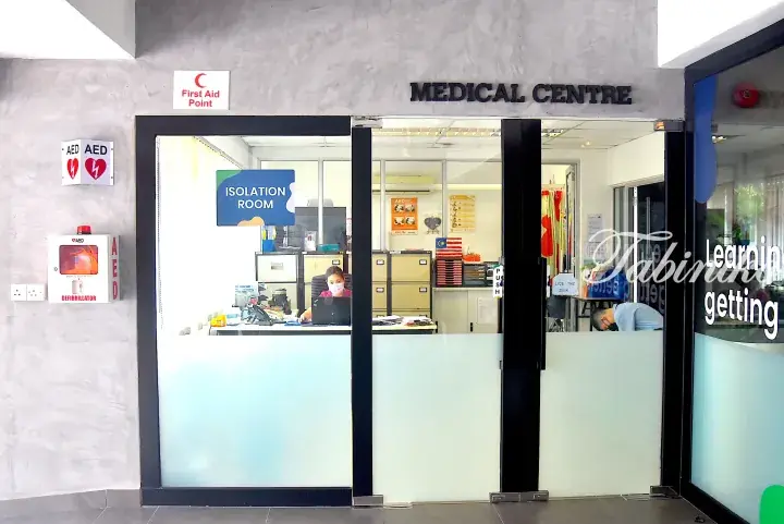 Medical centre entrance with glass doors, AED cabinet, and isolation room sign visible inside.