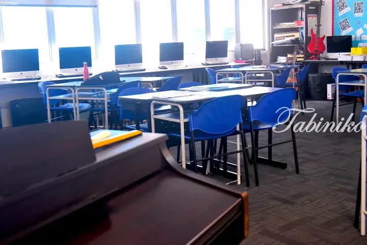 Modern classroom with blue chairs, desks, and computers, featuring a piano and musical instruments in the corner.