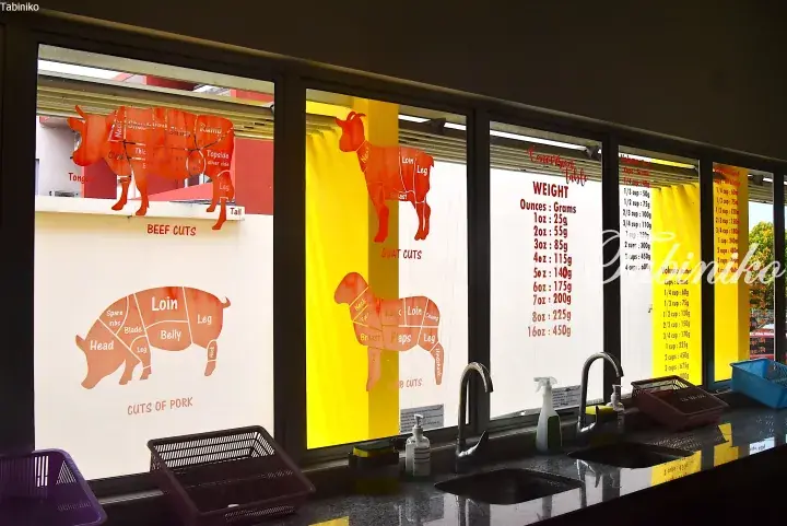 Window decals showing beef, pork, goat, and lamb cuts alongside weight conversion charts in a Malaysian kitchen.