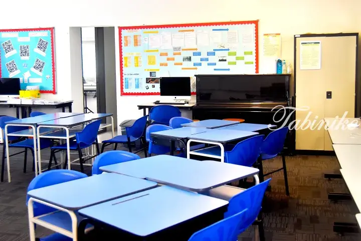 Empty music classroom with blue desks, chairs, a piano, and educational bulletin boards.