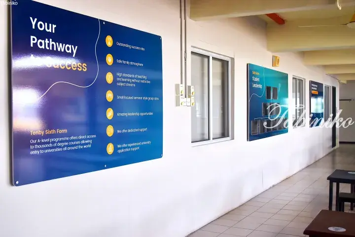 Blue informational sign at Tenby Sixth Form listing pathway to success features like outstanding success rate and safe family atmosphere.