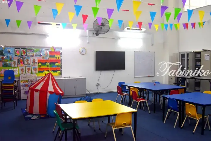 Colorful classroom with blue and yellow tables, chairs, a play tent, and festive bunting.