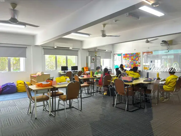 Students in yellow TENBY shirts attend an English class in a bright classroom with interactive whiteboard and learning materials.