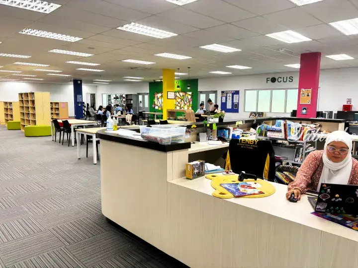Librarian at Tenby International School Setia Ecohill library desk with students studying in the background.